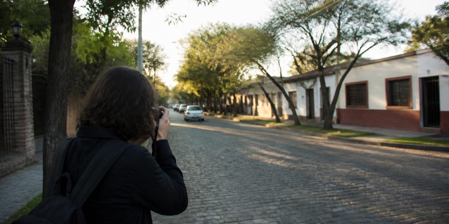 Persona fotografiando una calle arbolada del conurbano bonaerense