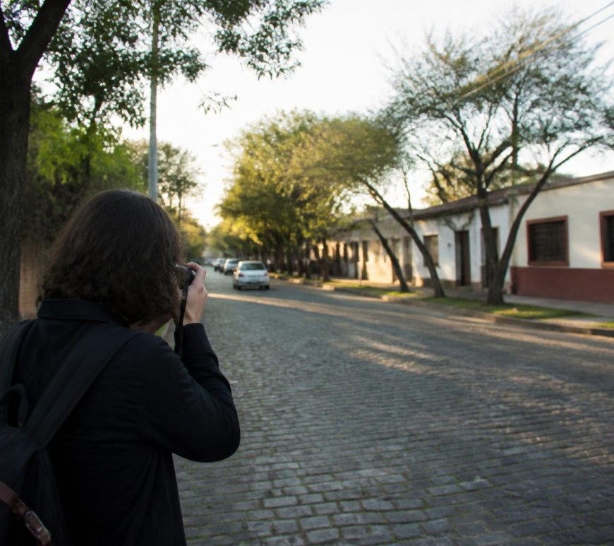 Persona fotografiando una calle arbolada del conurbano bonaerense