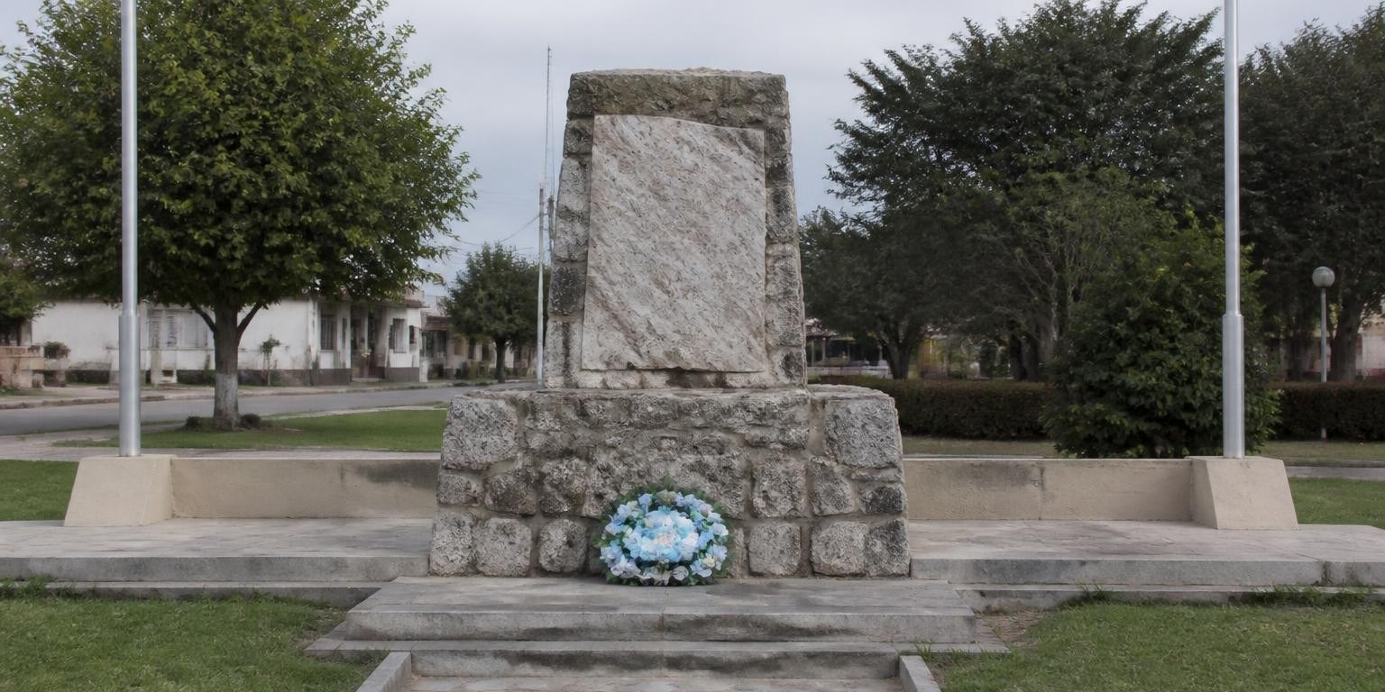 Plaza con un memorial sencillo y una ofrenda floral